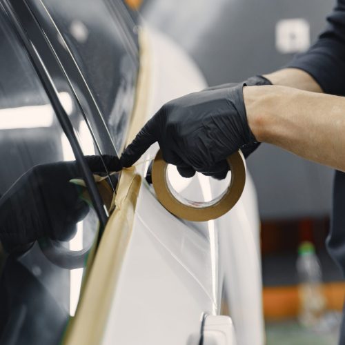 Auto body repair series. Masking car before repaint. Man in a black uniform.